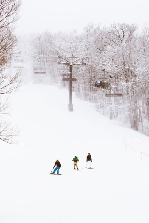 Hometown Christmas bucket list item - skiers and snowboarders ride down the local mountain enjoying the snow during the holiday season.