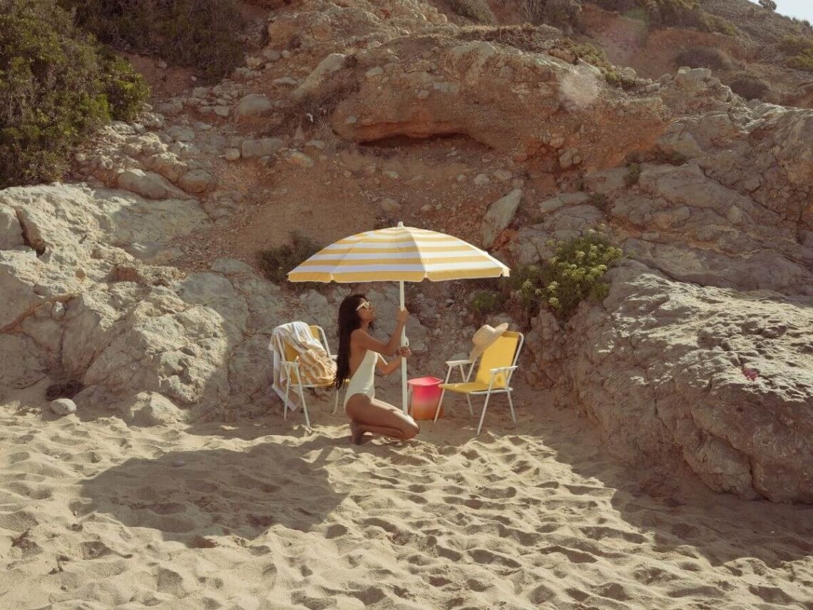 woman setting up beach umbrella to enjoy the sunny day at the beach