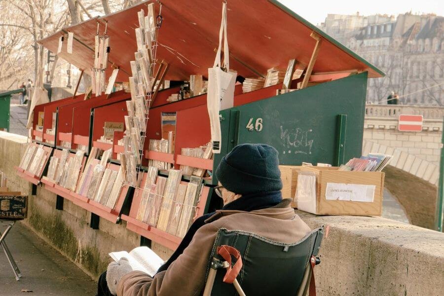 old man sitting and reading at bouquinistes (green book stalls) along the Seine. A UNESCO World Heritage site